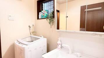 A bathroom with a washing machine, a sink, a mirror, and a window with a plant.