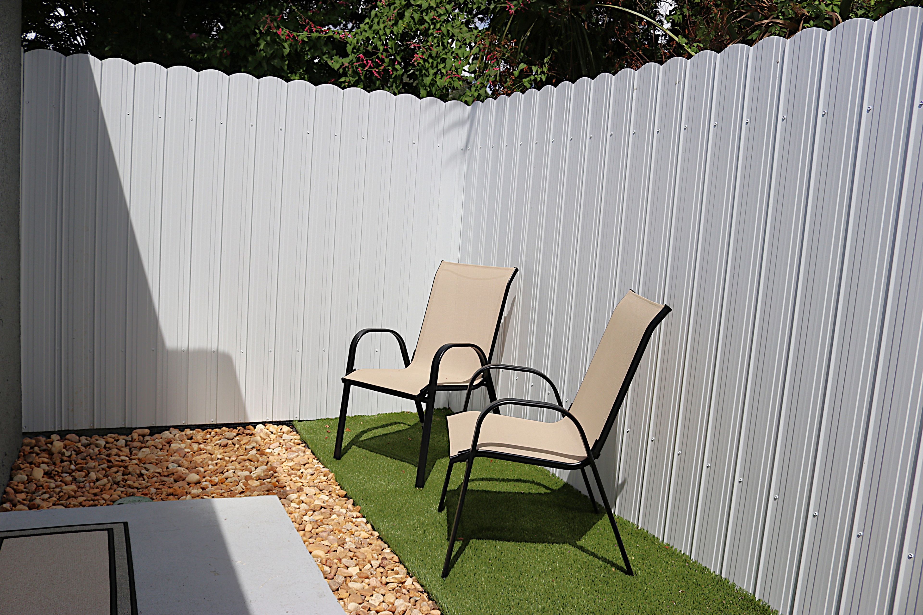 A patio area with two chairs and a table, surrounded by a white fence.