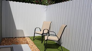 A patio area with two chairs and a table, surrounded by a white fence.