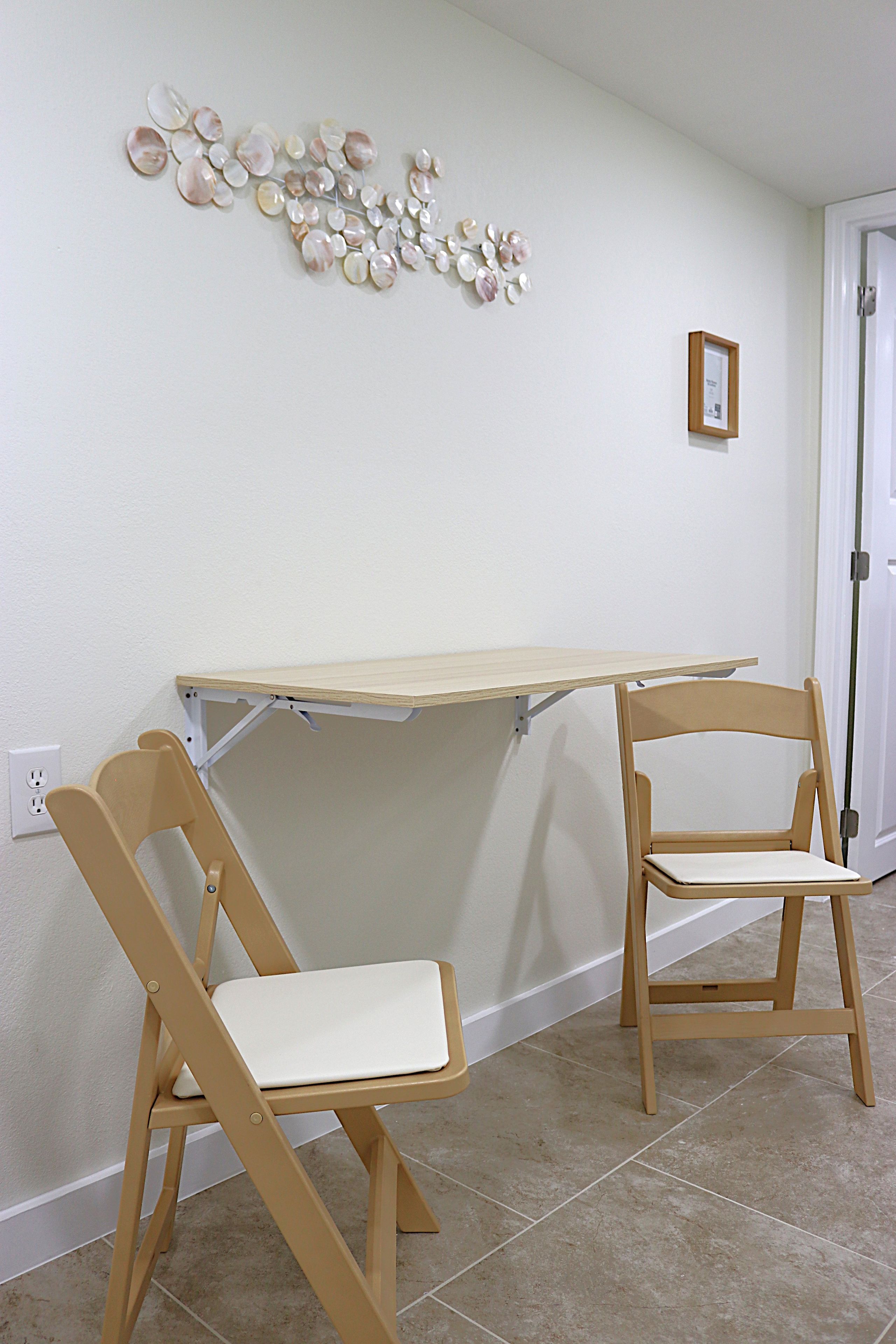 A room with a small table and two chairs, a wall-mounted decorative piece, and a door.