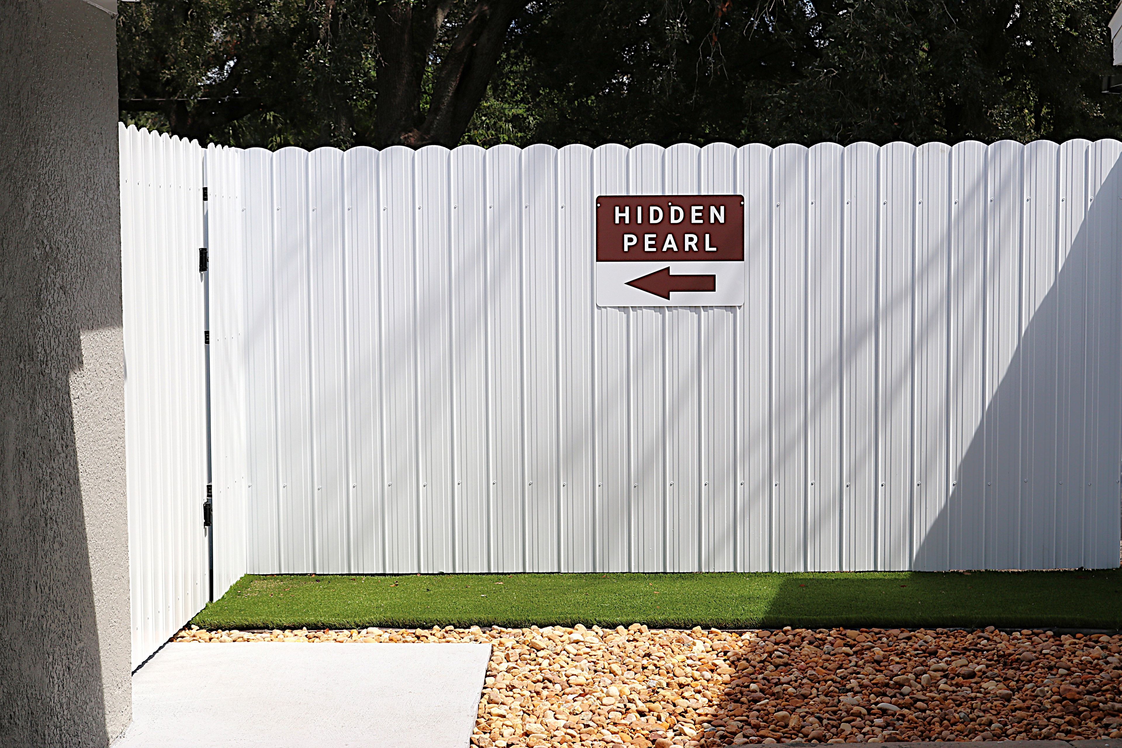 A white corrugated metal fence with a sign that reads 'HIDDEN PEARL' and an arrow pointing to the left.