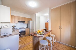 A compact kitchen with wooden cabinets, a built-in oven, a refrigerator, and a breakfast setup with two stools. - GuestReady - Nautilus La Restinga (La Restinga)