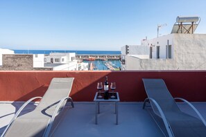 A rooftop terrace with two lounge chairs, a table with a bottle of wine and glasses, and a view of a marina with boats and the sea. - GuestReady - Nautilus La Restinga (La Restinga)