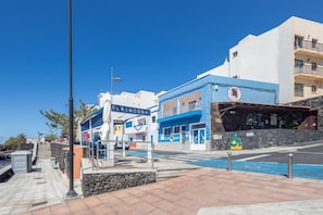A coastal street with buildings, a clear sky, and a blue-painted building with a sign. - GuestReady - Nautilus La Restinga (La Restinga)