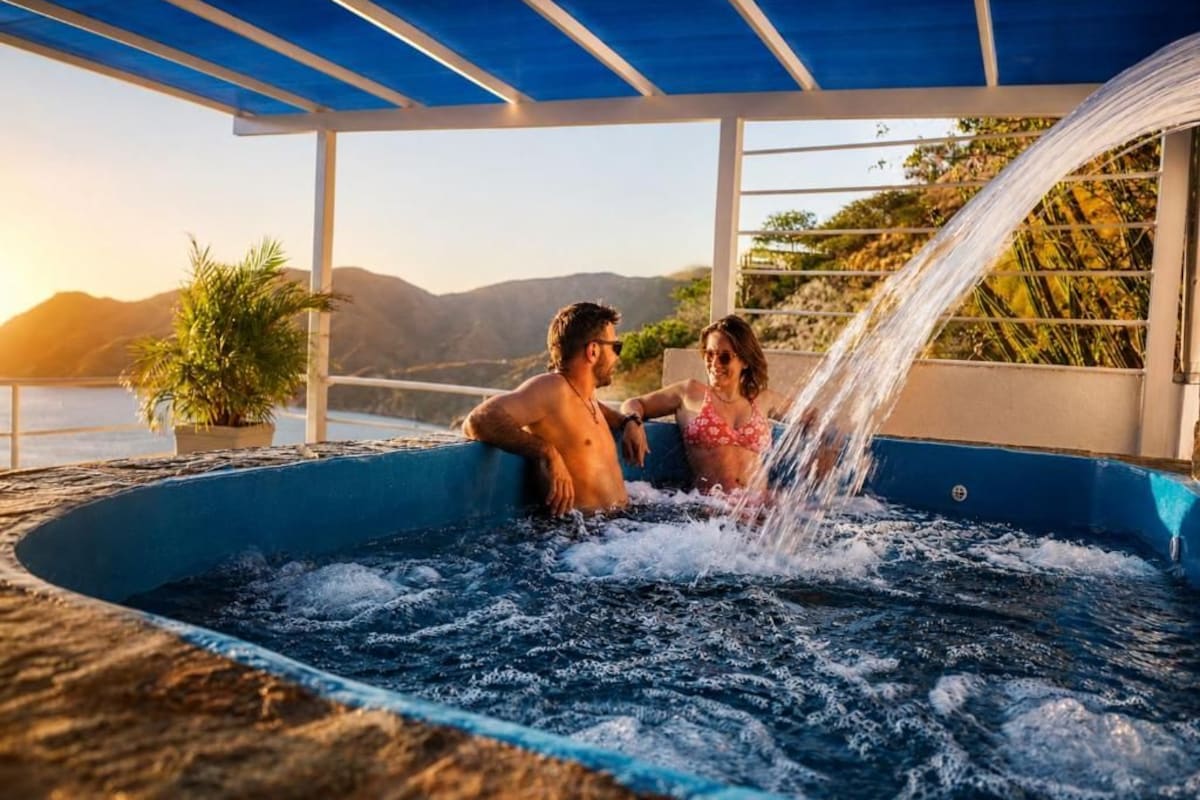 Una pareja en un jacuzzi con vistas a montañas y un cuerpo de agua.