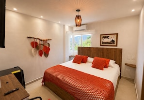 Un dormitorio con cama, cabecero de madera, aire acondicionado instalado en la pared, ventana con vistas y un adorno en la pared.