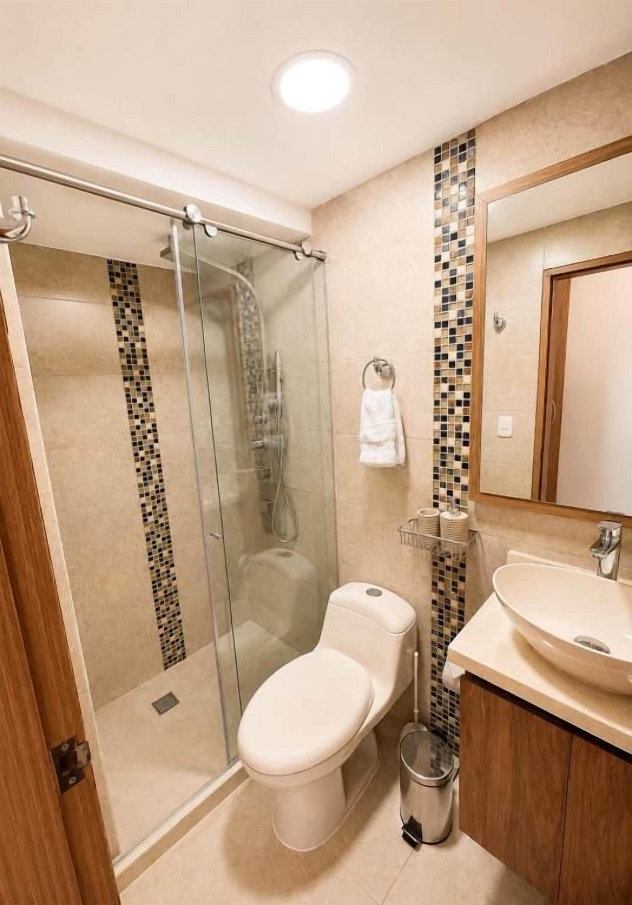 Une salle de bain avec une douche à parois de verre, des toilettes, un lavabo et un miroir.