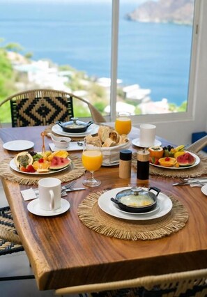 A breakfast table with plates of food, a cup, and a glass of orange juice, set against a view of the sea. - jaba nemaku boutique hotel (Santa Marta)