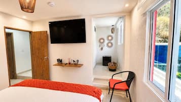 Ein Schlafzimmer mit einem Bett, einem Sessel, einem Fernseher, einem Regal mit Dekoration und einem Fenster mit Blick.