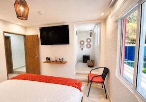 A bedroom with a bed, a chair, a TV, a shelf with decorative items, and a window with a view. - jaba nemaku boutique hotel (Santa Marta)