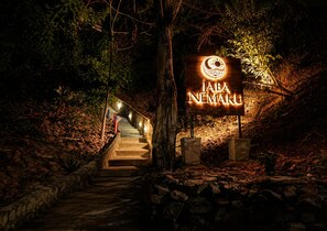 Una escalera de madera que lleva a un letrero que dice 'JABA NEMAKU BOUTIQUE HOTEL', con barandas y pared de piedra.