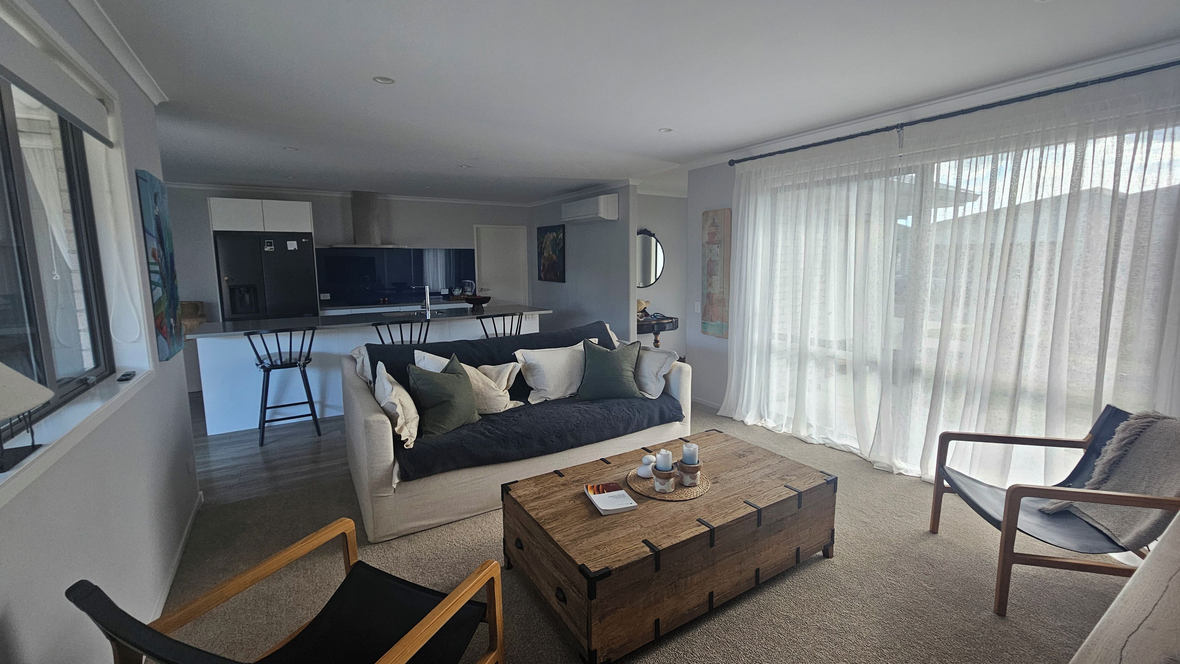 Een woonkamer met een bank, salontafel en stoelen. In de achtergrond is een keuken zichtbaar.