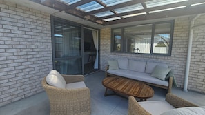 Une terrasse extérieure avec une porte vitrée donnant sur un coin repas, un canapé et des fauteuils en osier.