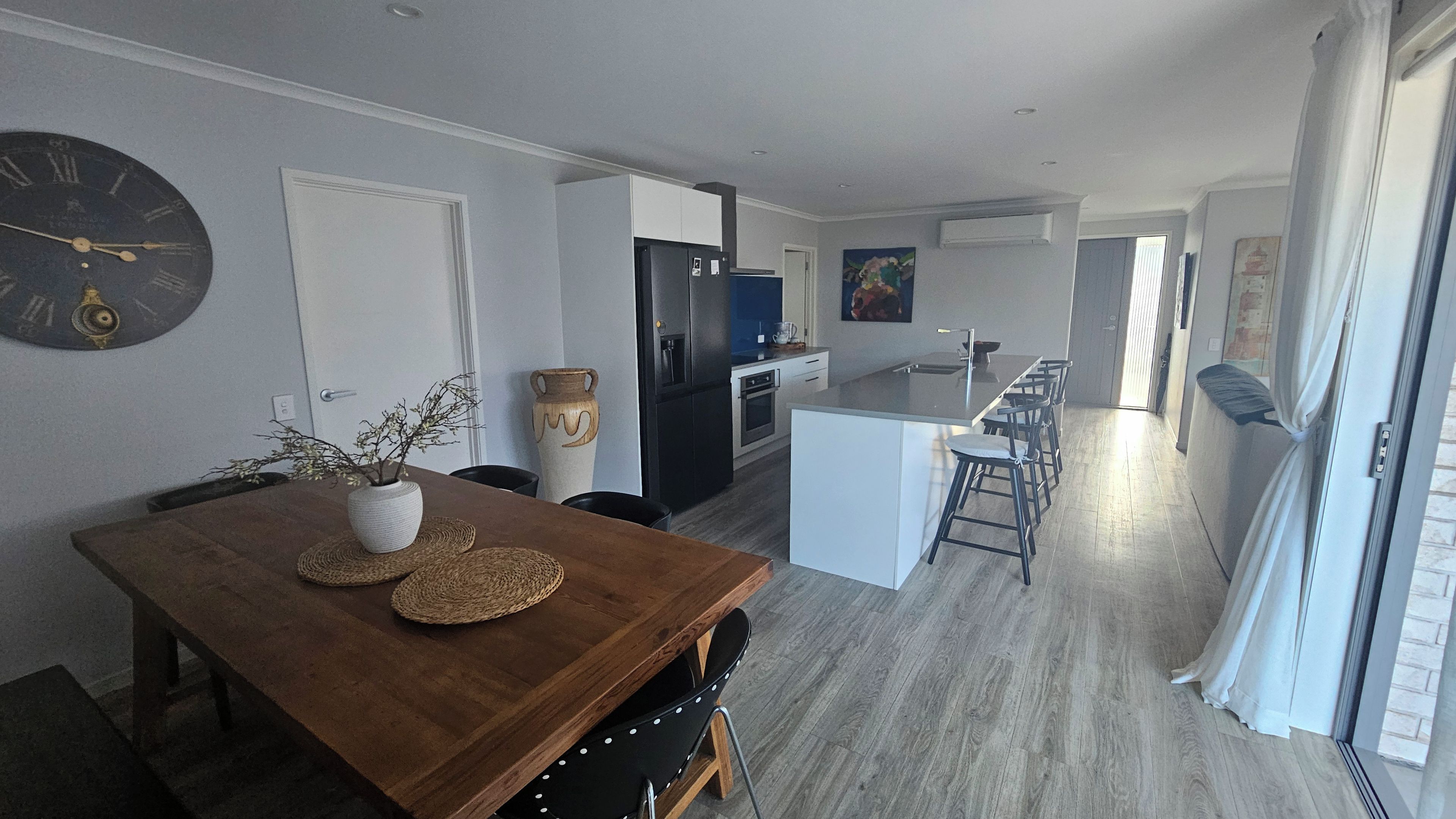 Een moderne keuken met een centraal eiland, een eethoek met een houten tafel en een zithoek met een bank en televisie.