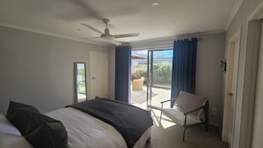Une chambre à coucher comprenant un lit, une chaise, un ventilateur de plafond et une porte-fenêtre coulissante donnant sur un patio.