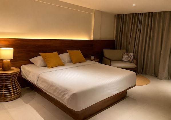 Habitación de hotel con una cama grande, una lámpara de noche, una silla y una cortina.