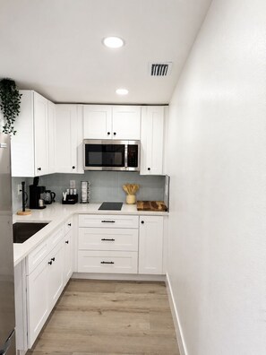 A modern kitchen with white cabinets, a stainless steel microwave, and a wooden countertop. - A First-Class Stay in Tampa Bay | Stadium, Midtown, and Downtown (Tampa)