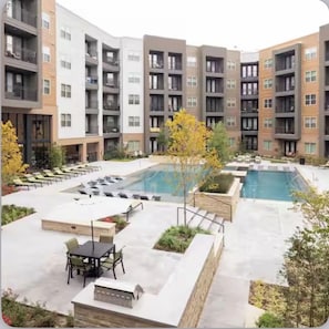 A modern apartment complex with a central swimming pool, outdoor seating, and a patio area. - The Luxe Oasis, Resort Pool, Near Grandscape & The Star (Lewisville)