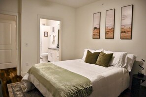 A bedroom with a bed, pillows, a bedside table, and a nightstand. There is a door leading to a bathroom. - The Luxe Oasis, Resort Pool, Near Grandscape & The Star (Lewisville)