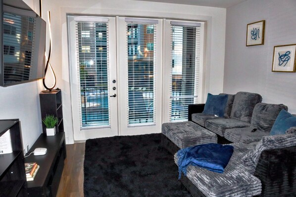 A living room with a black rug, grey sofa with blue cushions, a black side table with a plant, and a framed picture on the wall. - The Luxe Oasis, Resort Pool, Near Grandscape & The Star (Lewisville)