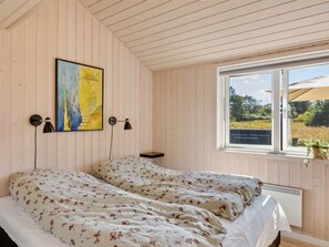 Ein Schlafzimmer mit einem Bett, einem Fenster, einem Gemälde und einer Wandlampe.