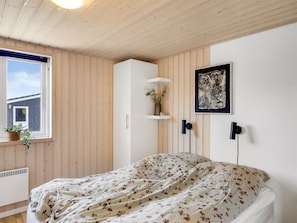 A bedroom with a bed, a window, a plant, a shelf with decorative items, and a framed artwork on the wall. - "Fokke" - 900m from the sea by Interhome (Løkken)