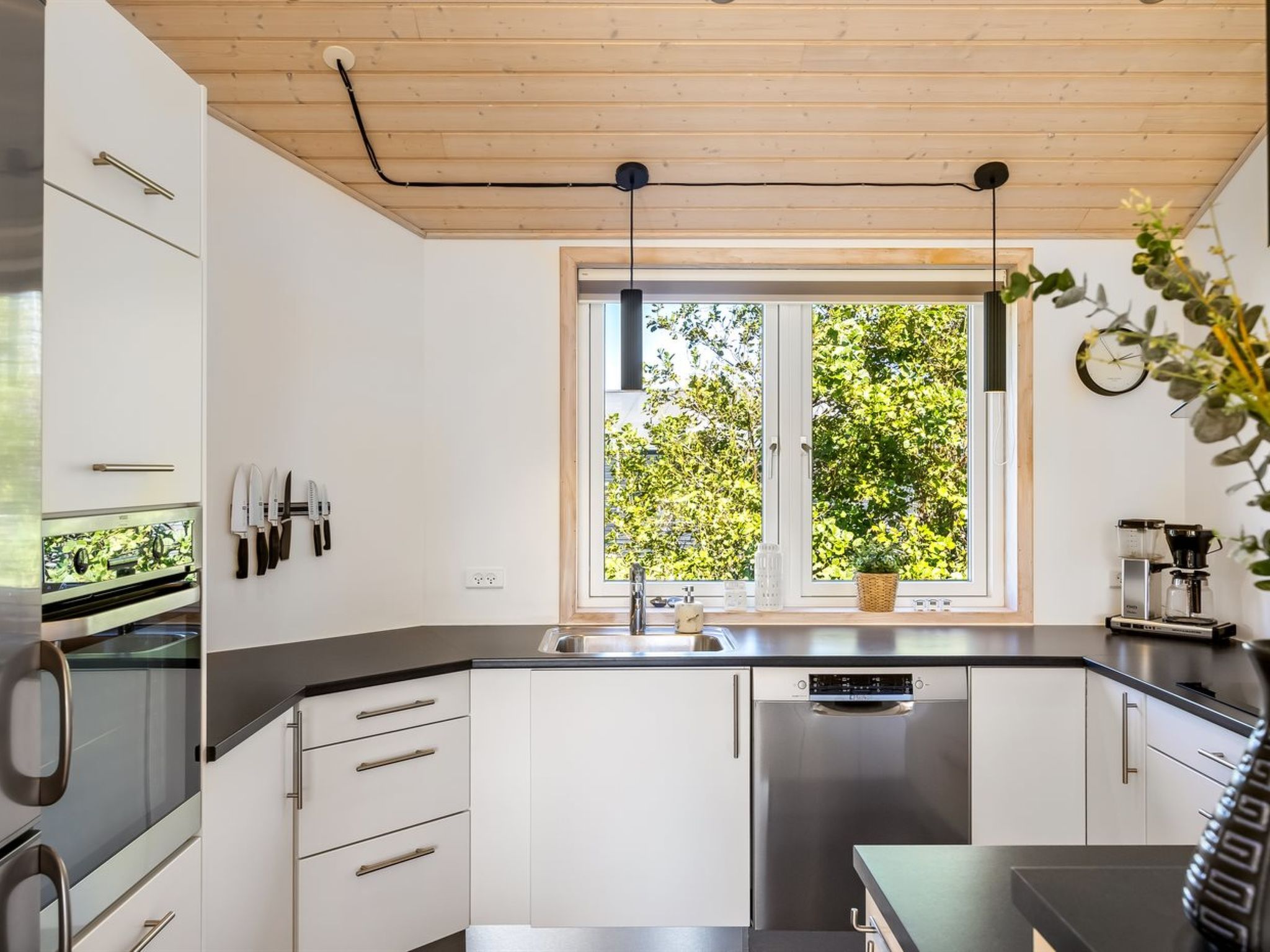 A modern kitchen with white cabinets, stainless steel appliances, and a window with a view of greenery.