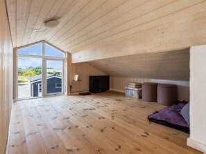 A room with a sloped ceiling, wooden flooring, a television, and a large window offering a view of solar panels outside. - "Fokke" - 900m from the sea by Interhome (Løkken)