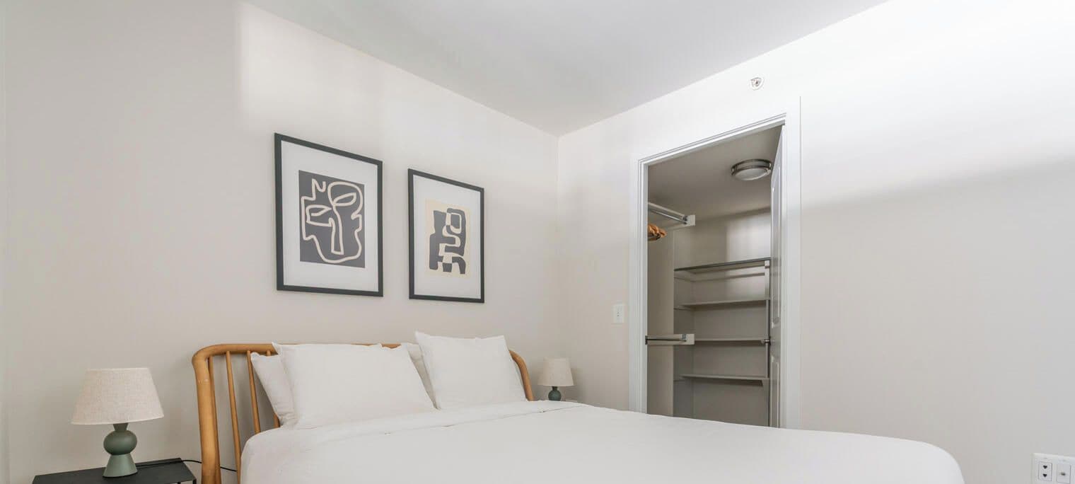 A bedroom with a bed, two bedside tables with lamps, a wardrobe, and two framed artworks on the wall.