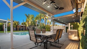 Un patio exterior con una mesa y sillas, una piscina y una zona cubierta con ventilador de techo.