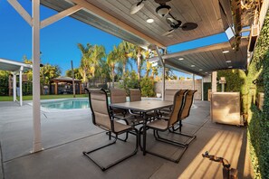 Une terrasse extérieure avec une table et des chaises, une piscine et un espace abrité doté d’un ventilateur de plafond.
