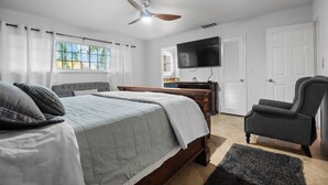 Un dormitorio con cama, una silla, televisor y ventilador de techo.
