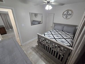 Une chambre à coucher avec un lit, un ventilateur de plafond, une porte et un miroir fixé au mur.