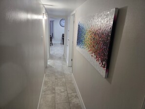 A hallway with a tiled floor, a clock on the wall, and a colorful abstract painting on the right. - Serene 3-bedroom house with AC in charming Chandler (Chandler)