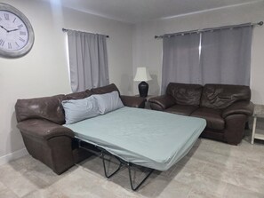 Una habitación con una cama, dos sofás marrones, una lámpara y un reloj de pared.