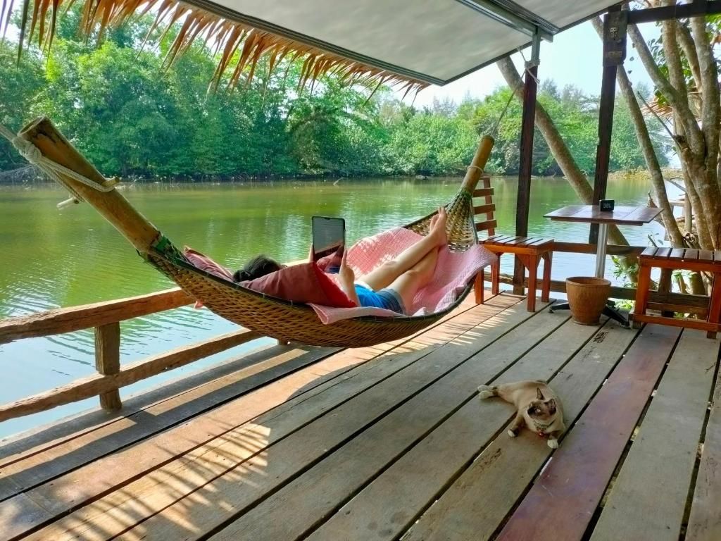 Una hamaca en una cubierta de madera con vistas a un cuerpo de agua, y un perro pequeño acostado cerca.