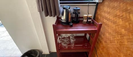 Una estantería de madera con una cafetera, frascos y vasos.