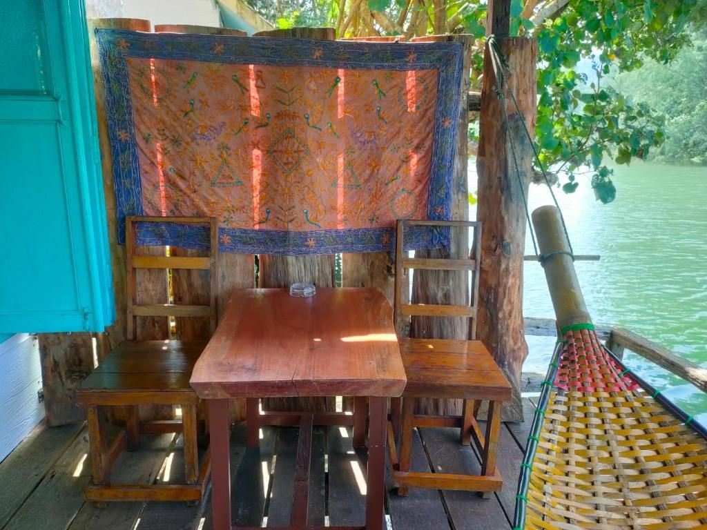 Terraza de madera con mesa y sillas, una silla tejida y vista al agua.
