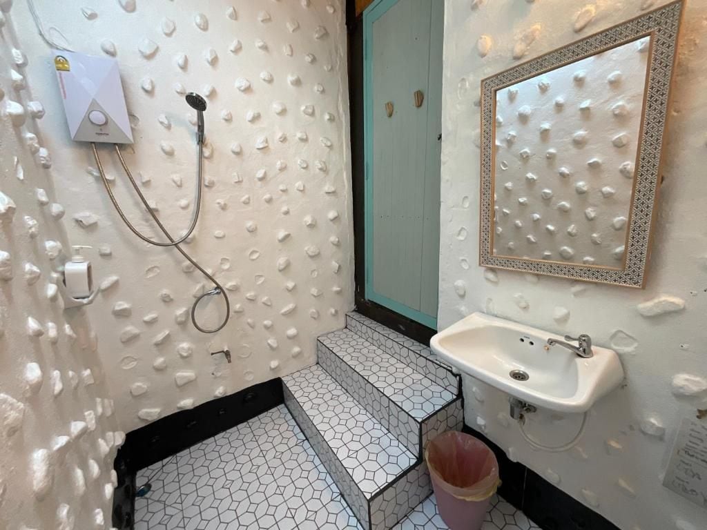 A bathroom with a white sink, a mirror with a decorative frame, and a shower area with textured walls.