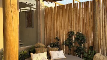 Pyöreä ulkotila, jossa on puinen pergola yläpuolella, bambuaita ympärillä ja pehmustettu penkki koristetyynyineen.
