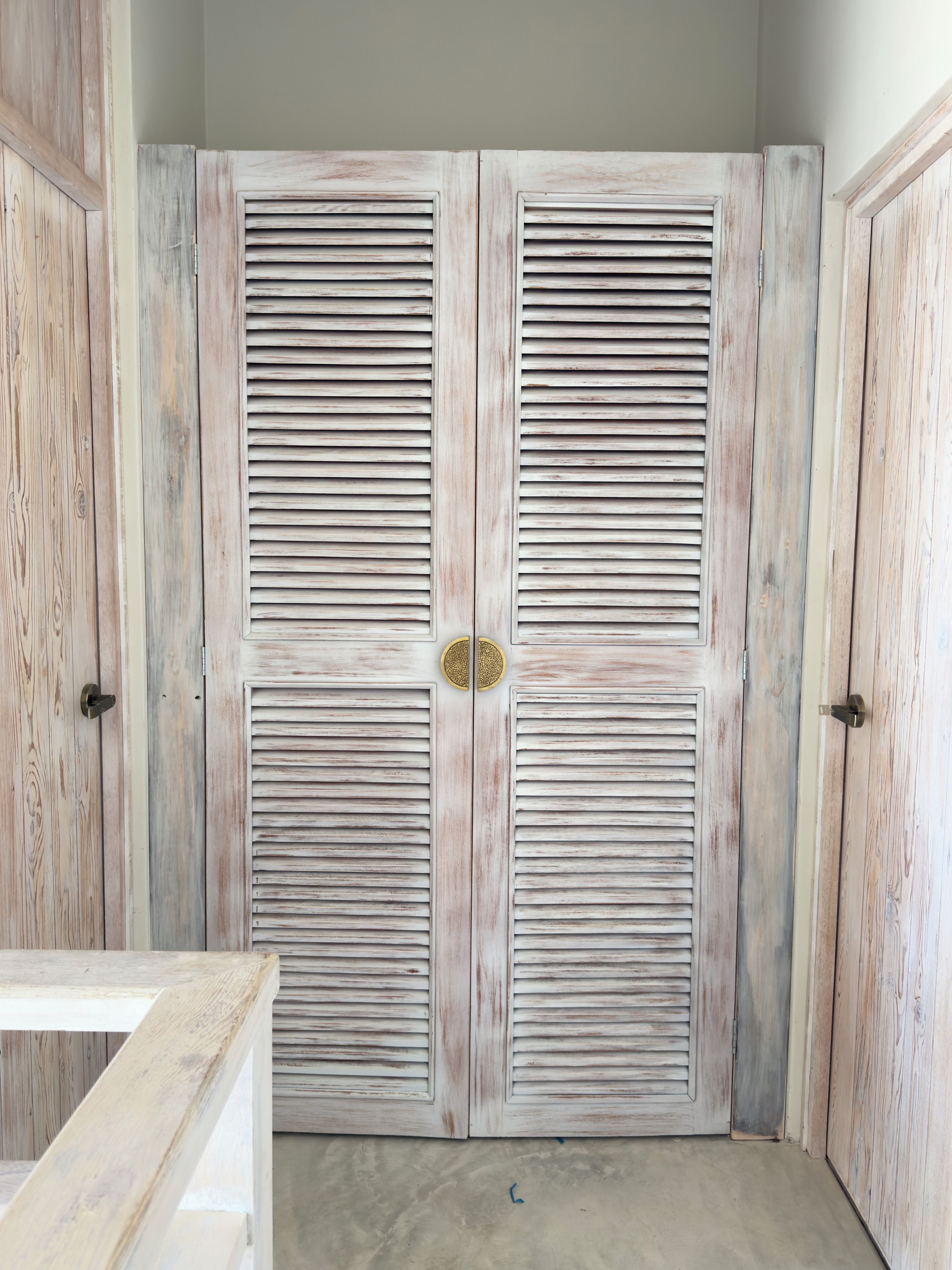 Un juego de puertas dobles con listones horizontales, un pomo de latón y una pequeña placa de latón en el centro.