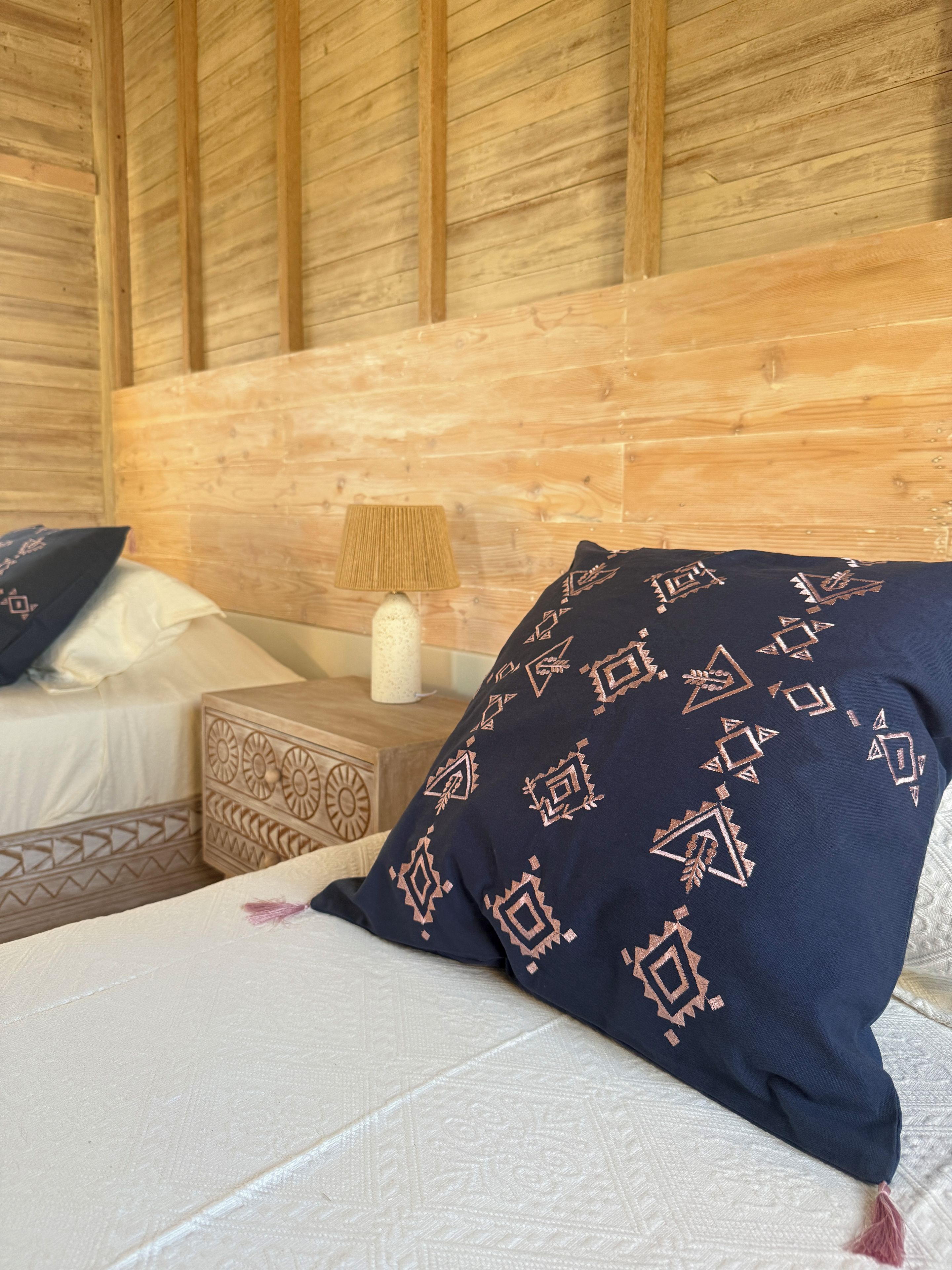 A bed with a patterned pillow, a bedside table with a lamp, and a wooden headboard.