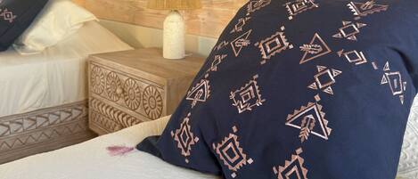 Una cama con un cojín estampado, una mesita de noche con una lámpara y un cabecero de madera.