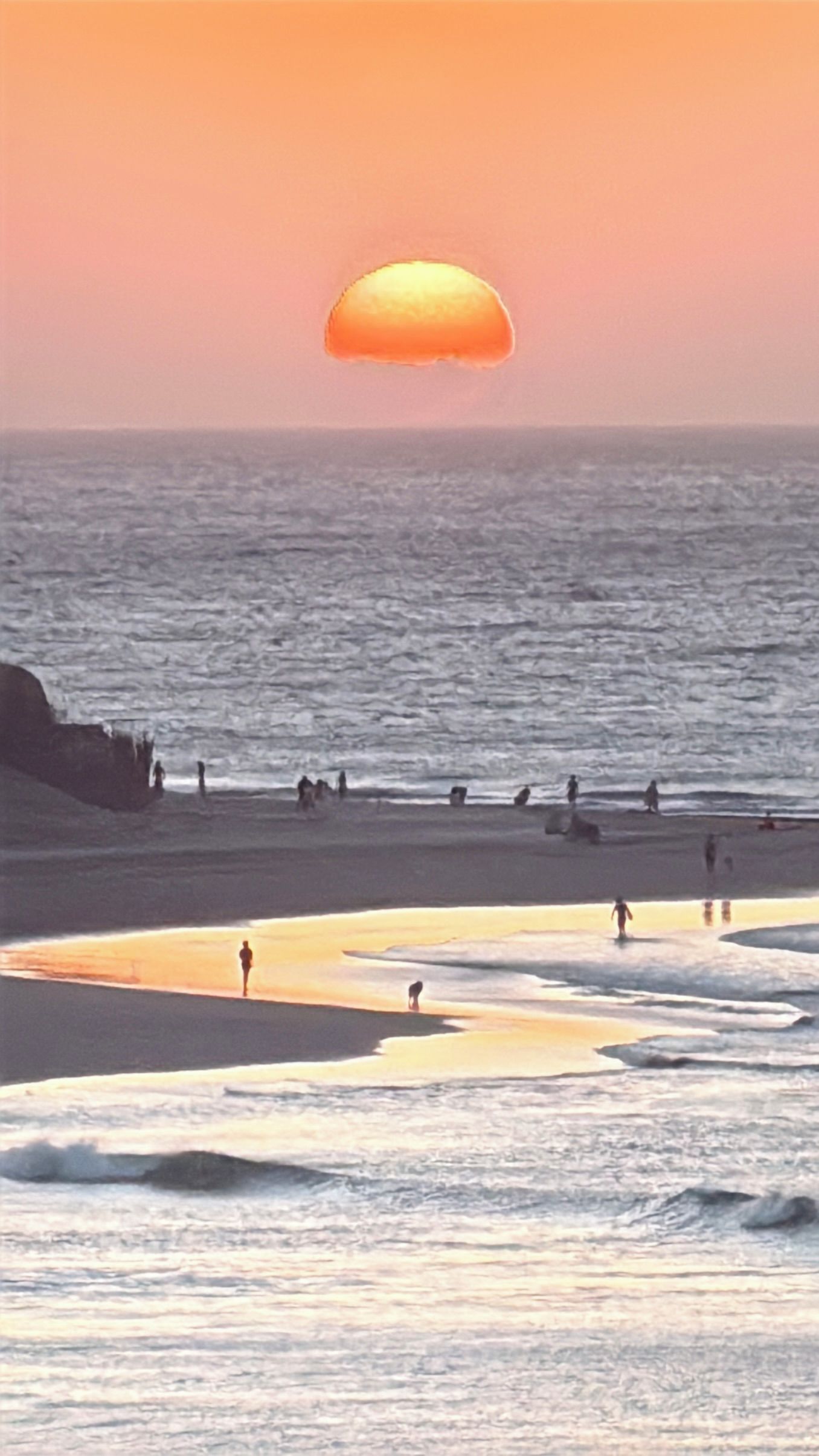 Escena de playa con atardecer, olas y gente.