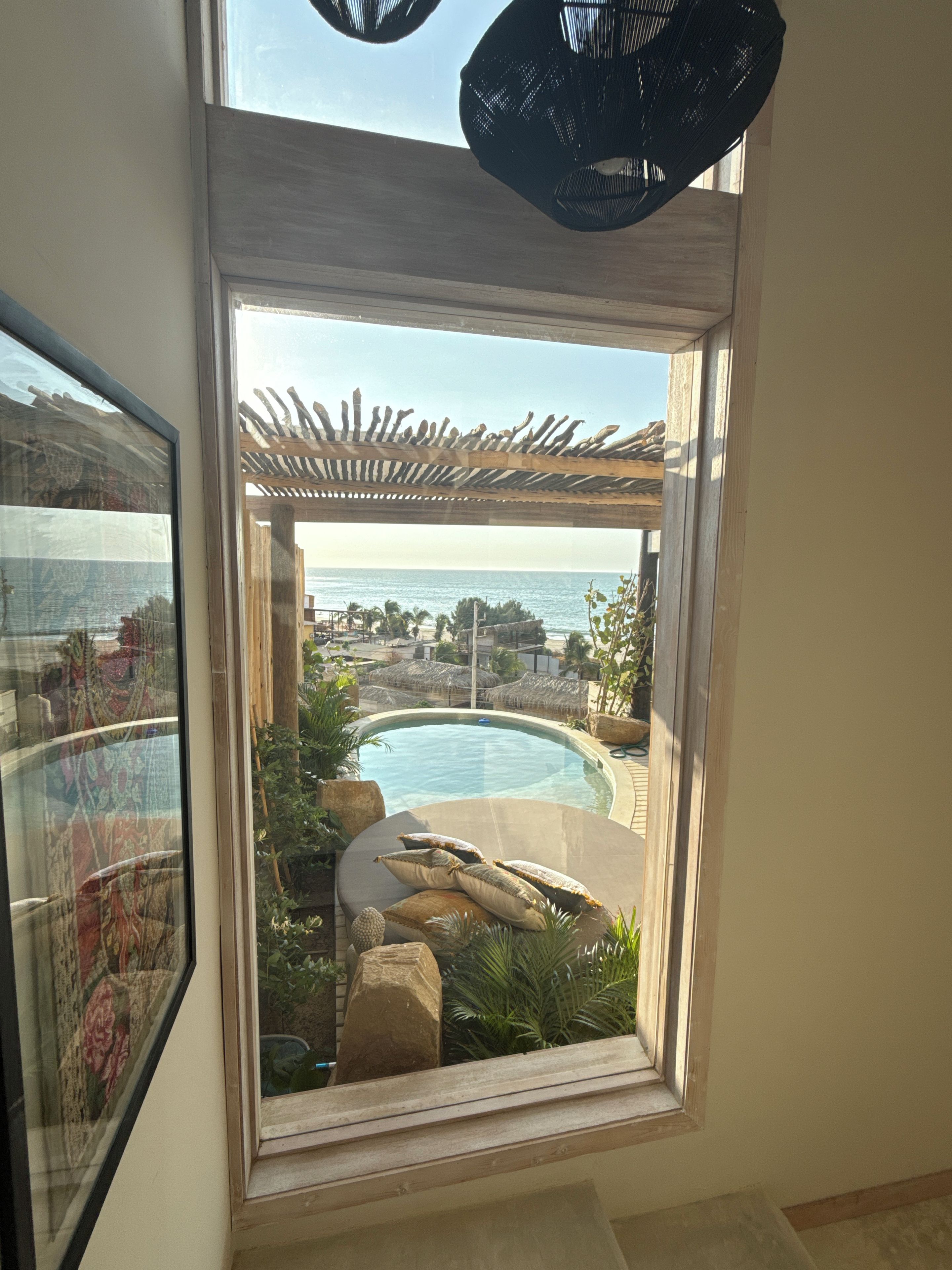 Vista a través de una ventana de un área de piscina con una pérgola, piscina y vista al océano.