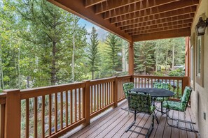 A wooden deck with a table and chairs, surrounded by a wooden railing, overlooking a forested area. - NEW 2BR w/ Hot Tub, Free Shuttle, Parking, WiFi (Vail)