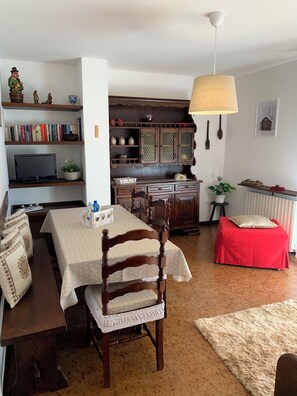Un saló acollidor amb una taula de menjador, cadires, un televisor, una biblioteca i una zona de cuina.