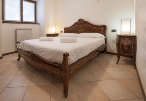 A bedroom with a wooden bed, two bedside lamps, a radiator, and a small table with a mirror. - AffittiPontediLegno - Casa Ruby (Ponte di legno)