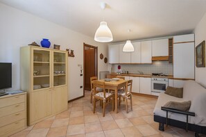 A compact living space with a dining table, chairs, a sofa, a kitchenette, and a television. - AffittiPontediLegno - Casa Ruby (Ponte di legno)