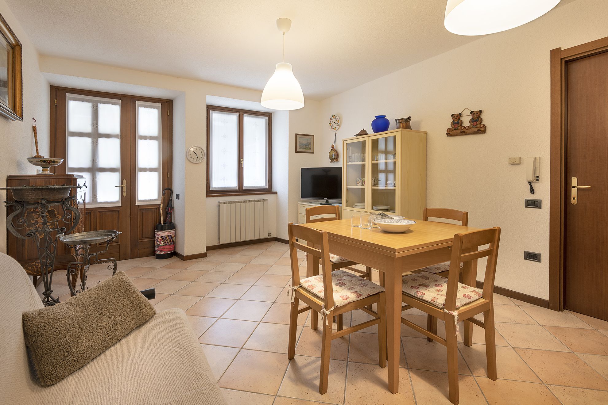 Un coin repas avec une table et des chaises en bois, un meuble avec des portes en verre, un téléviseur et une horloge au mur.